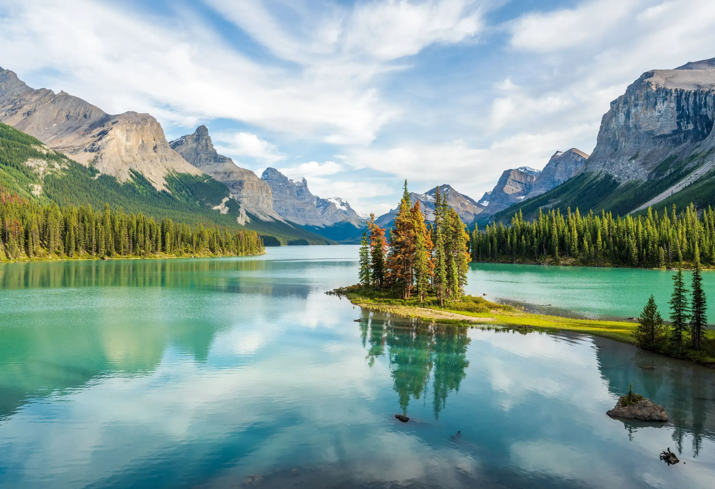 A lake with a centre island surrounded by forest and mountains.