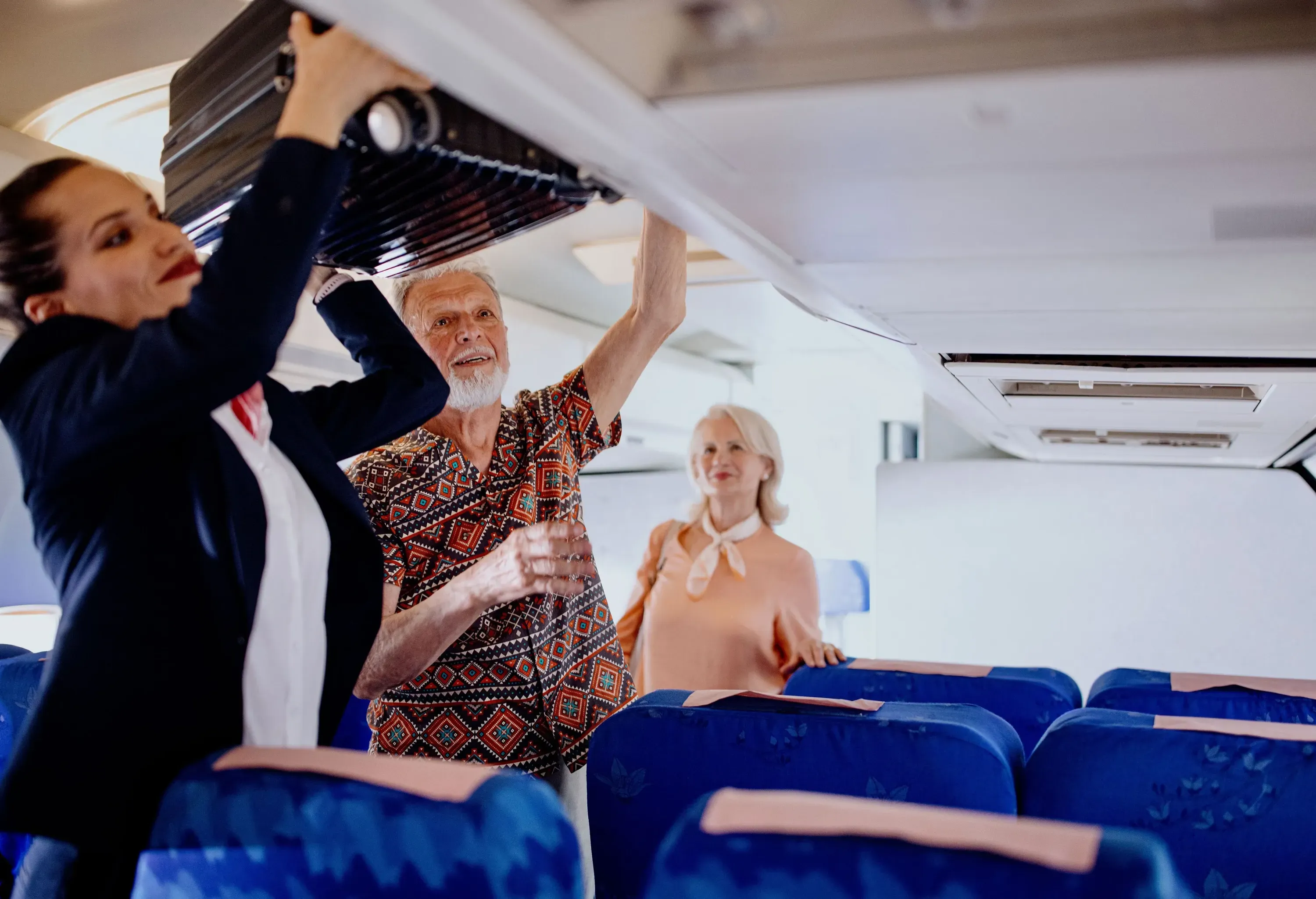 flight attendant placing a carry-on into the overhead bin