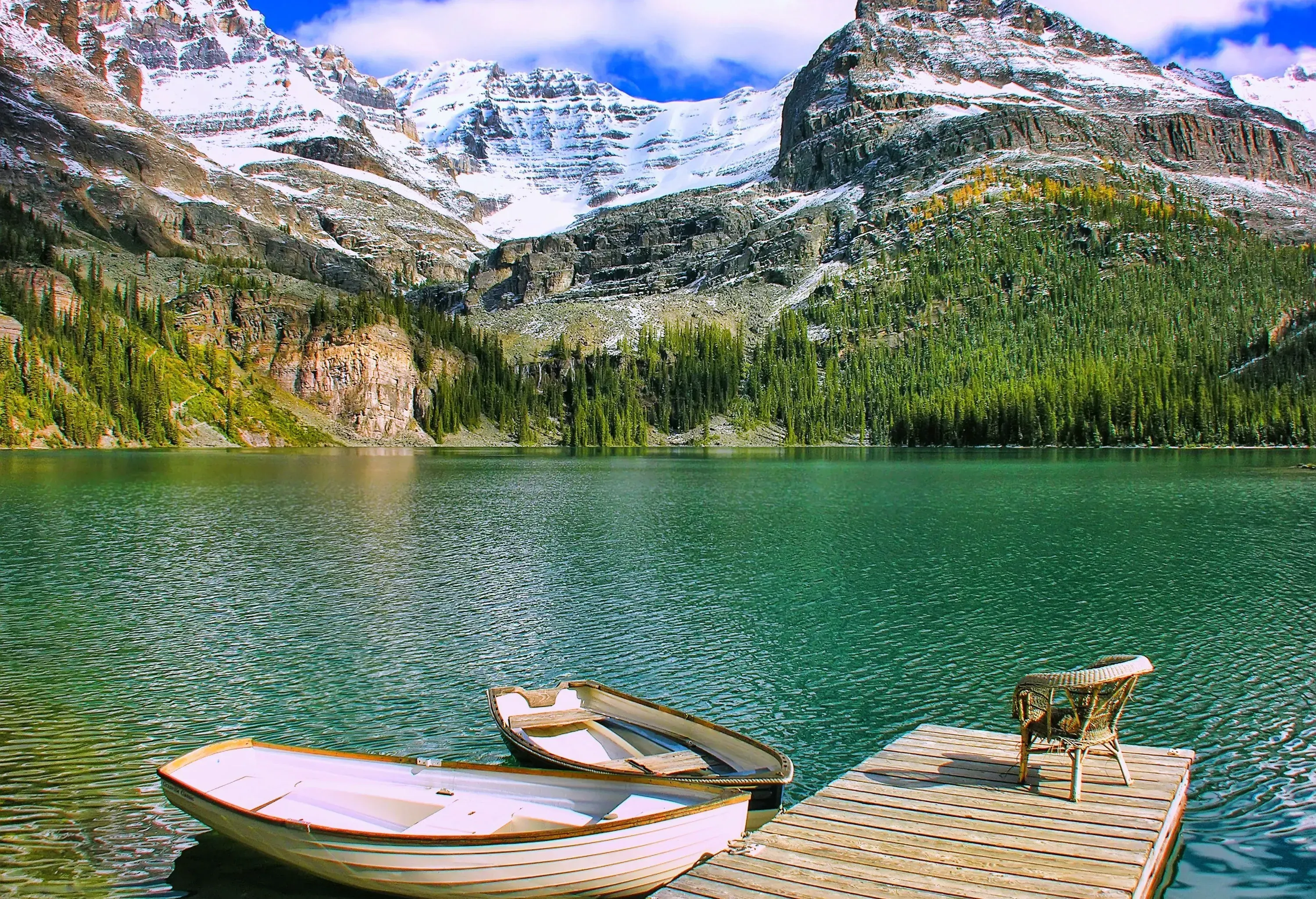 Two small boats tied on a dock beside a green water lake with trees along the foothill.