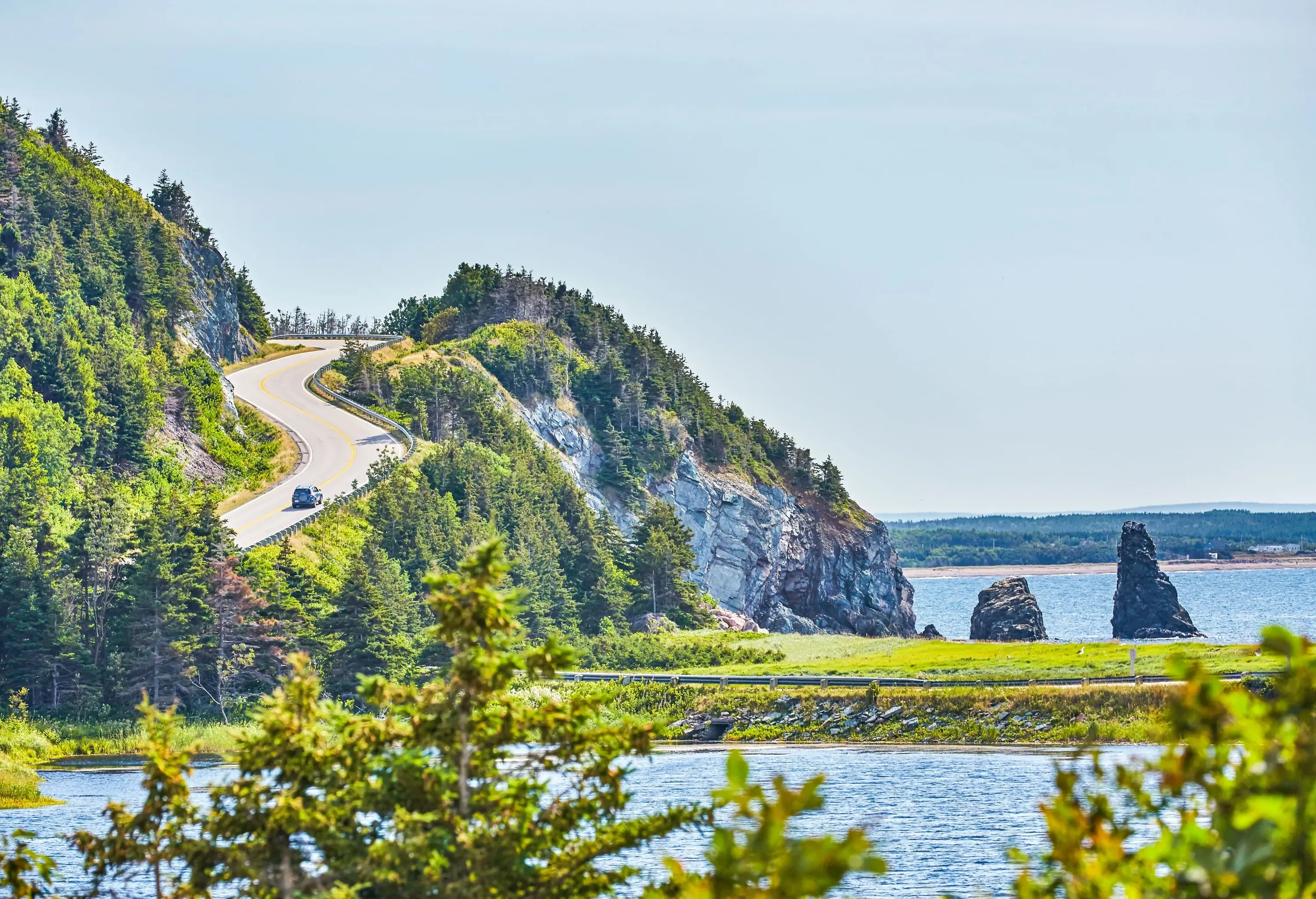 A car ascending a steep highway looping around a rock cliff overlooking the sea.