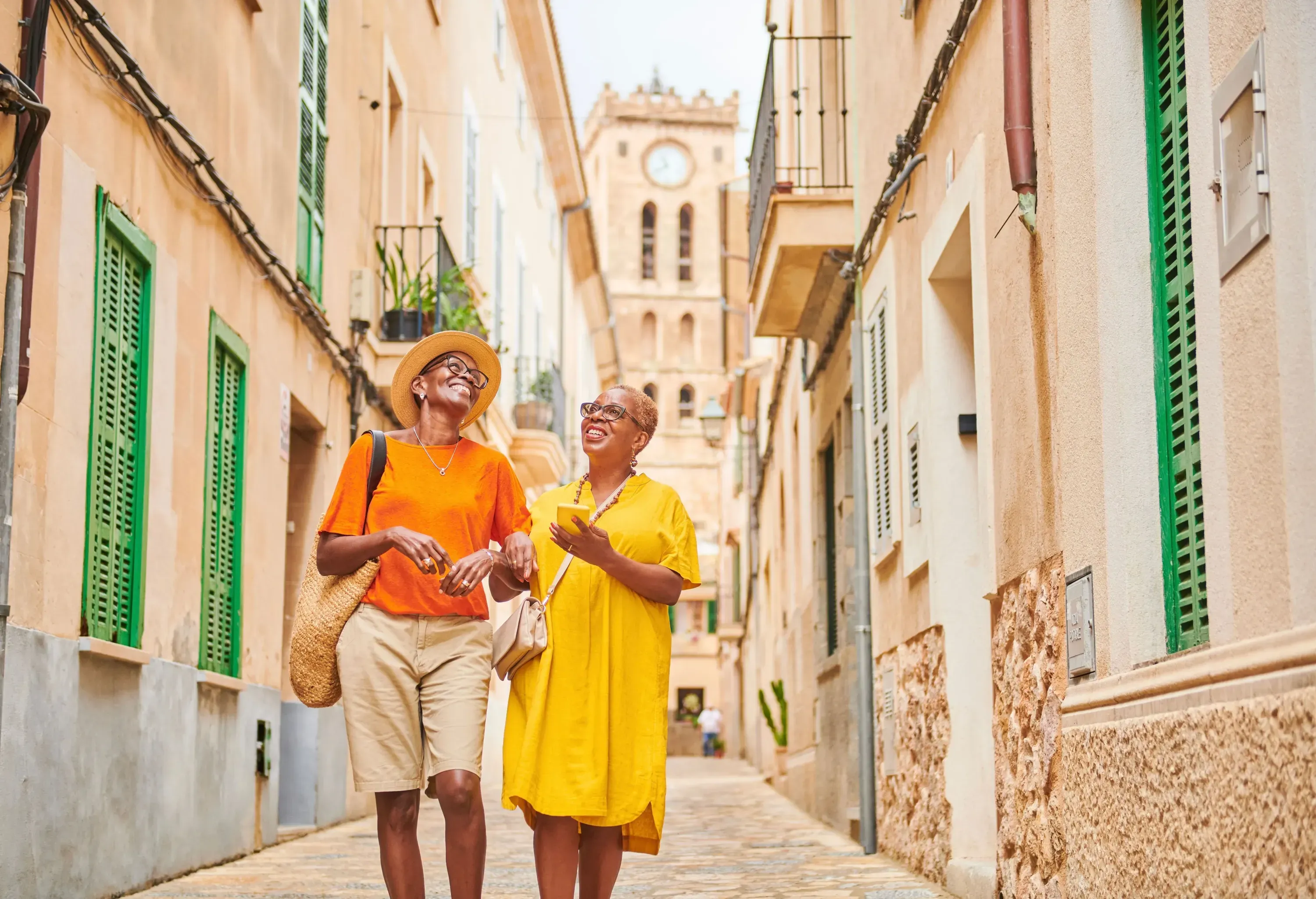 Two women both looking up with smiles while walking down a narrow street lined with traditional buildings.