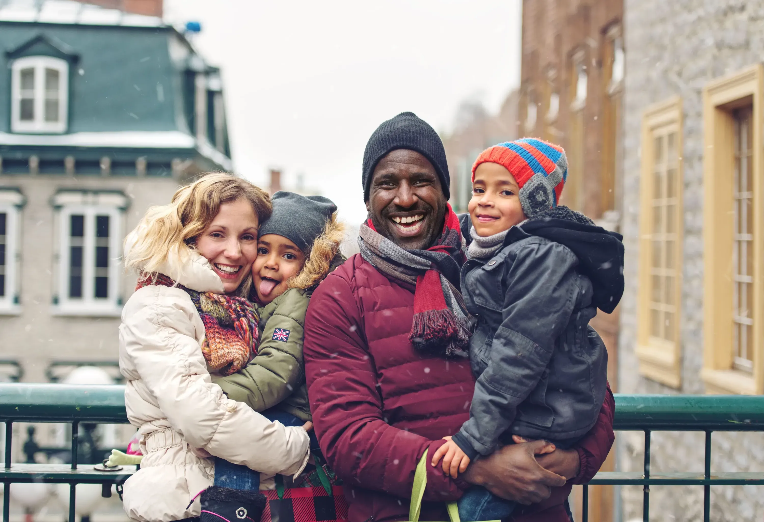 A couple dressed for the winter smiles as they carry their kids.