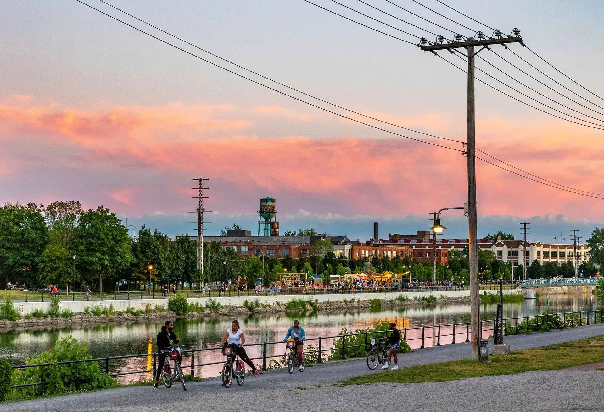 People biking and walking along a waterway at sunset