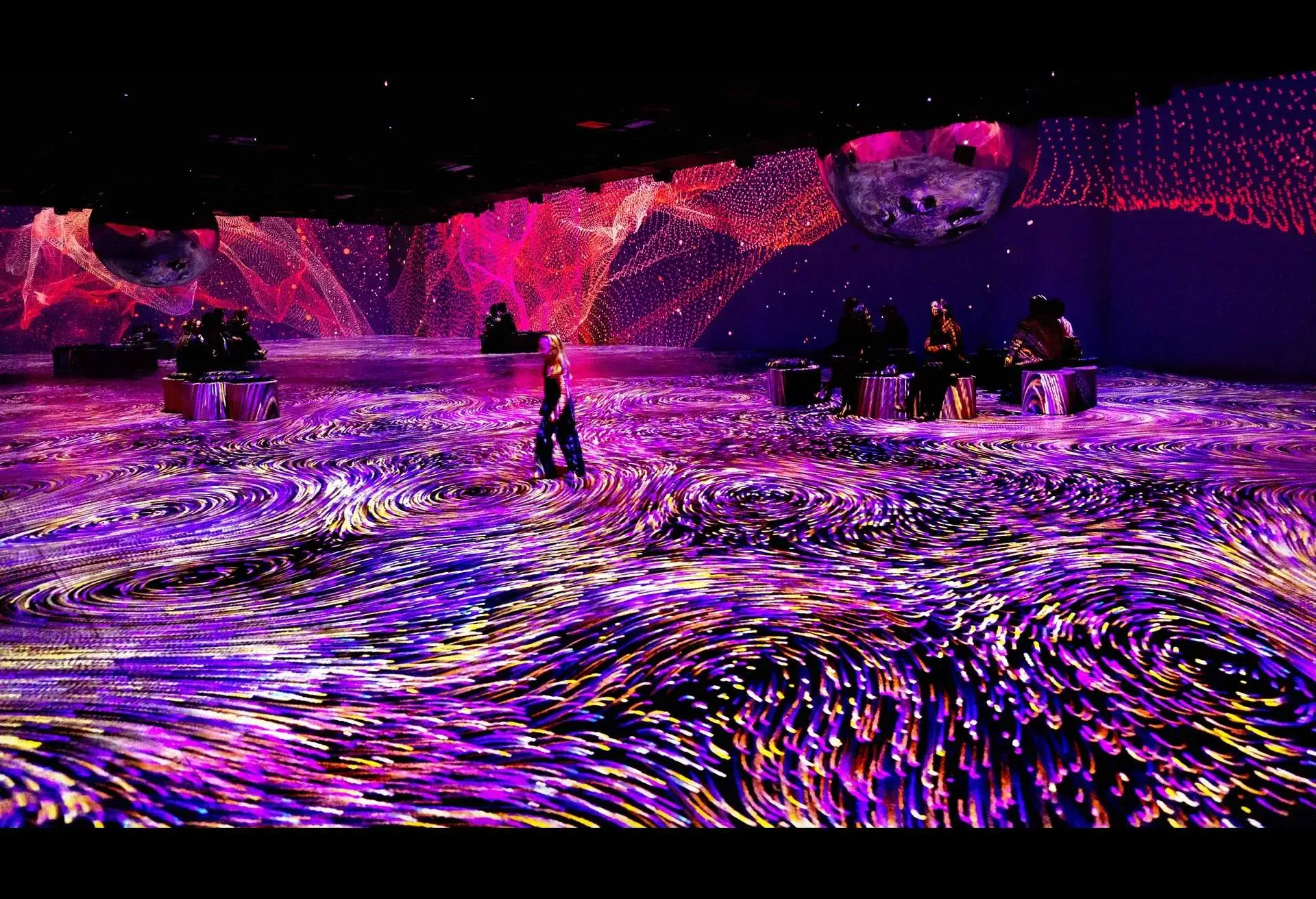 People dancing, enjoying vivid swirling visual art installation with purples and pinks under a dark ceiling