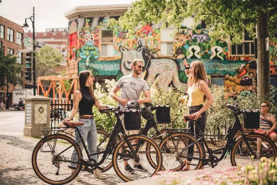 Cyclists talking in front of colorful mural with bikes on a sunny day.