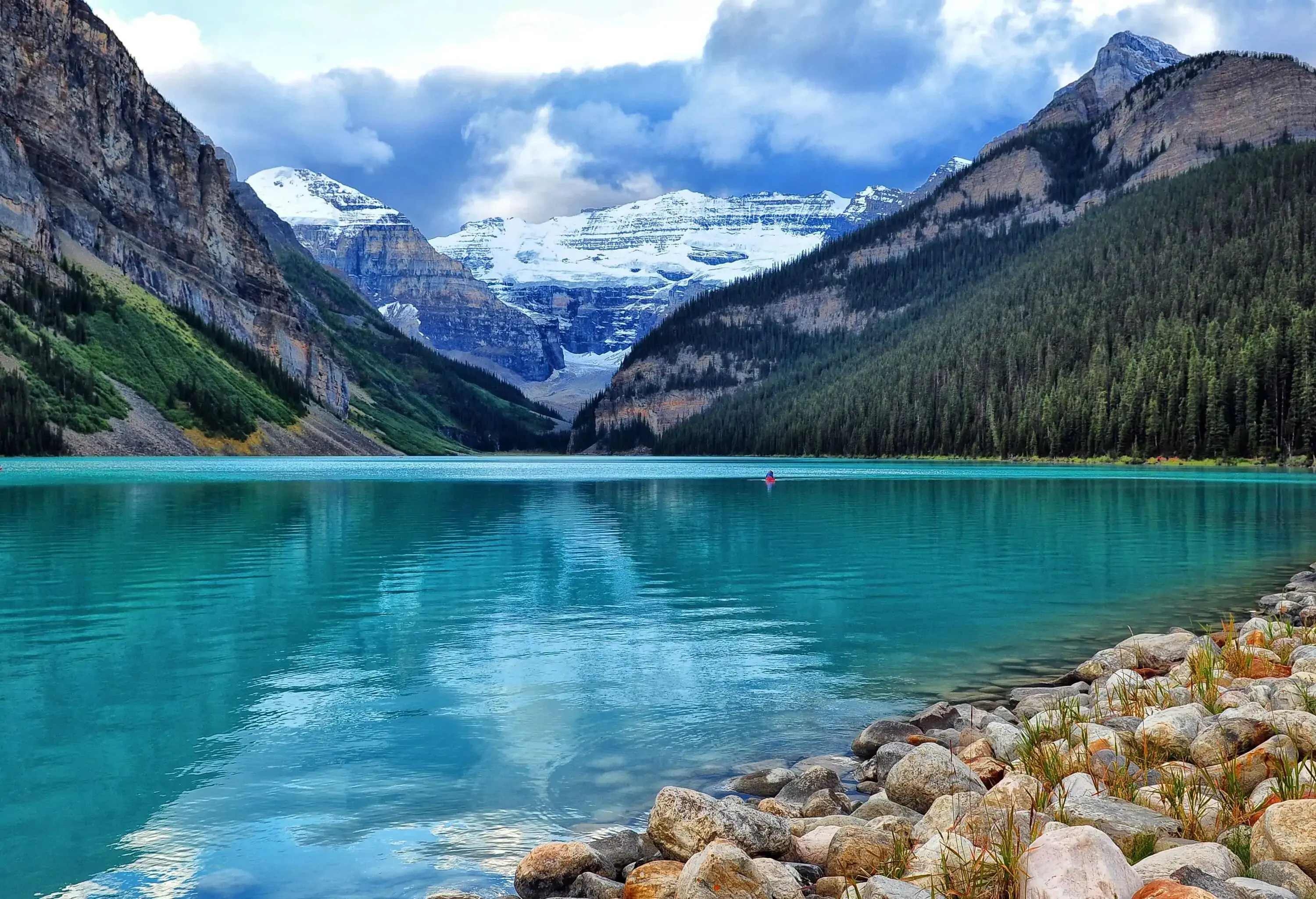 A picturesque lake surrounded by mountains with a boat sailing in the turquoise still water.