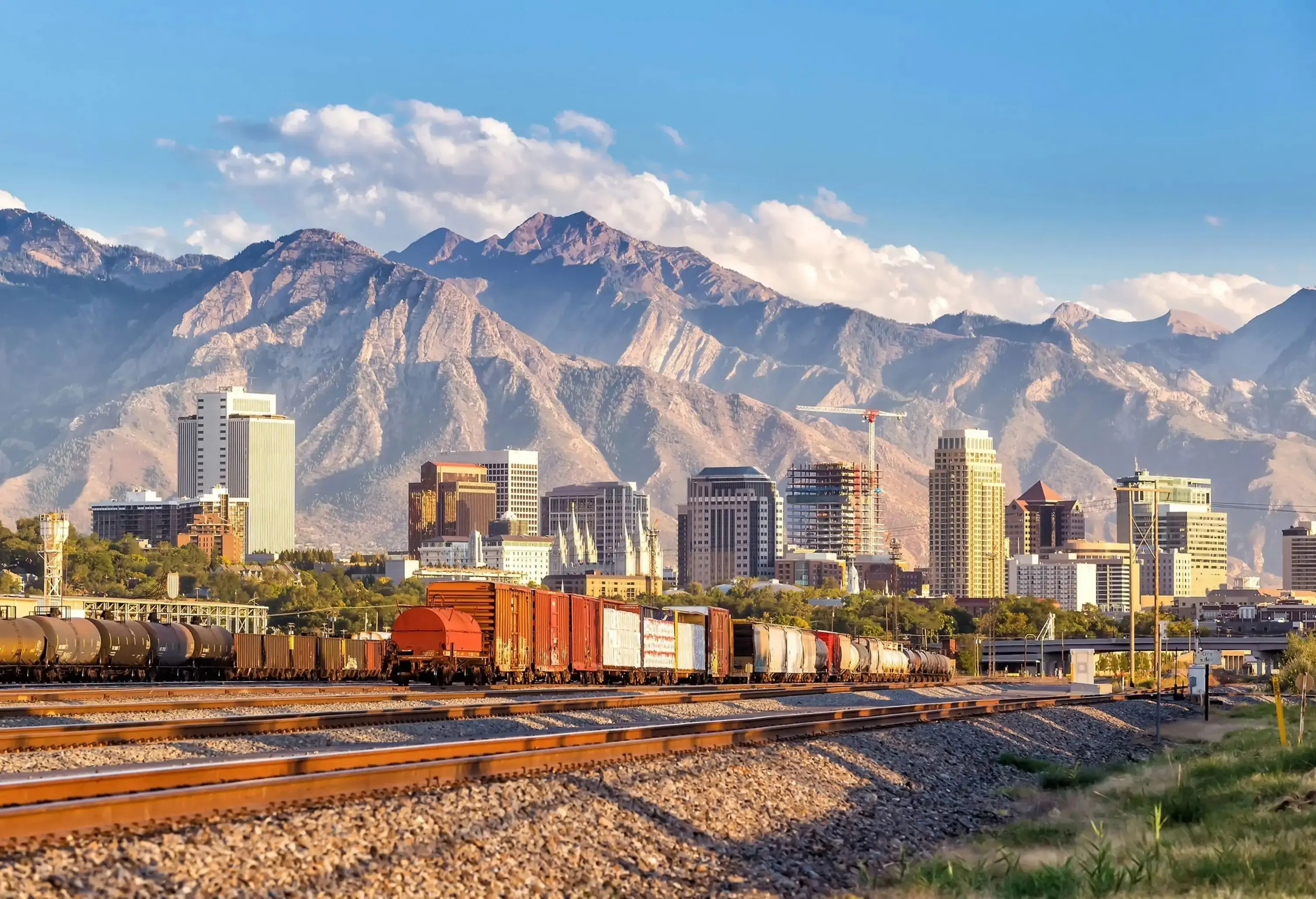 Old trains on a railway against the backdrop of the city skyline and rugged mountains.