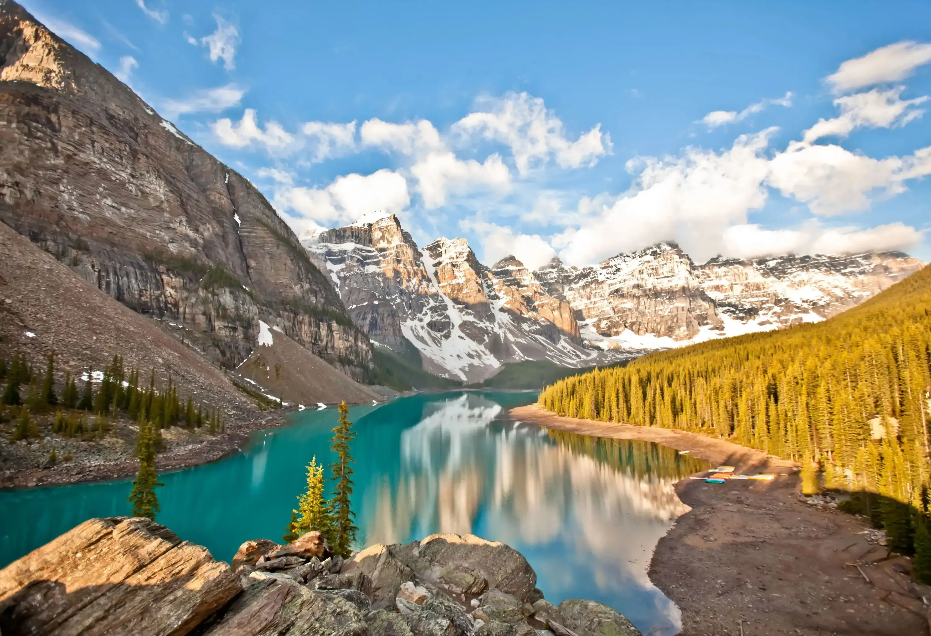 A lake surrounded by a pine forest and steep snowy mountains as seen from a rock summit.