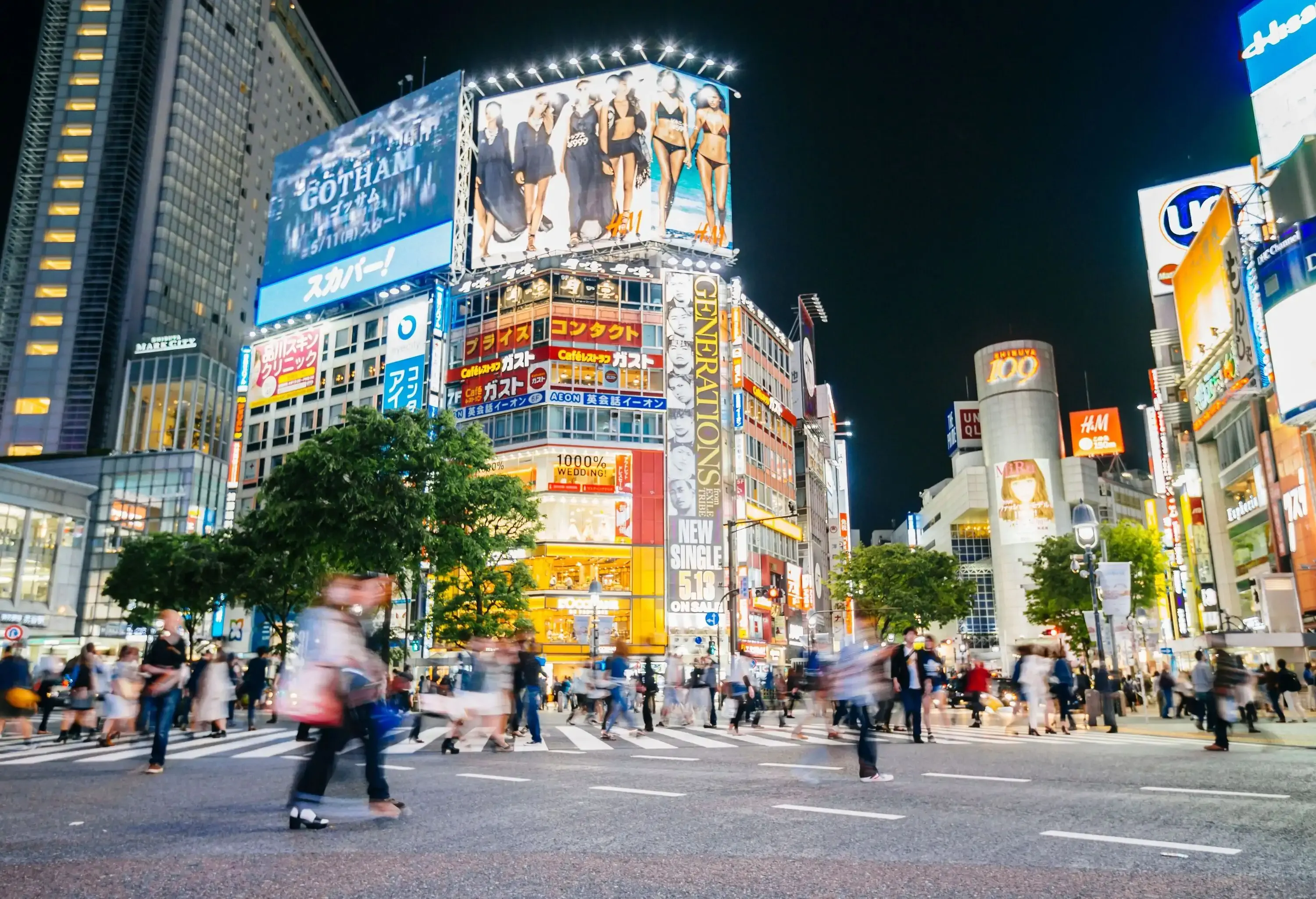 The heavily used scramble crossing at Shibuya with huge digital advertisements illuminating the building façades. 