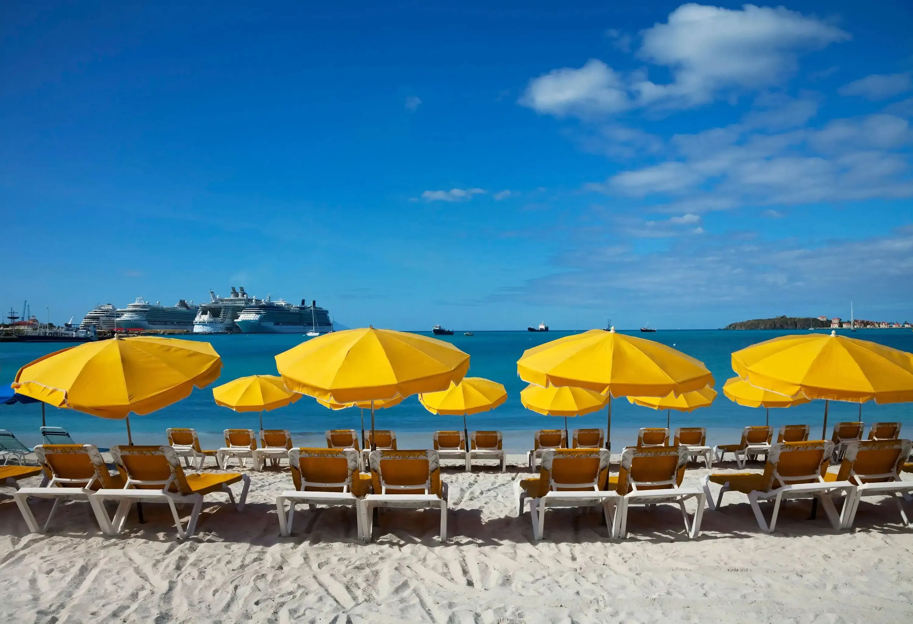 Rows of bright yellow umbrellas and sun loungers across a sandy beach facing the sea.