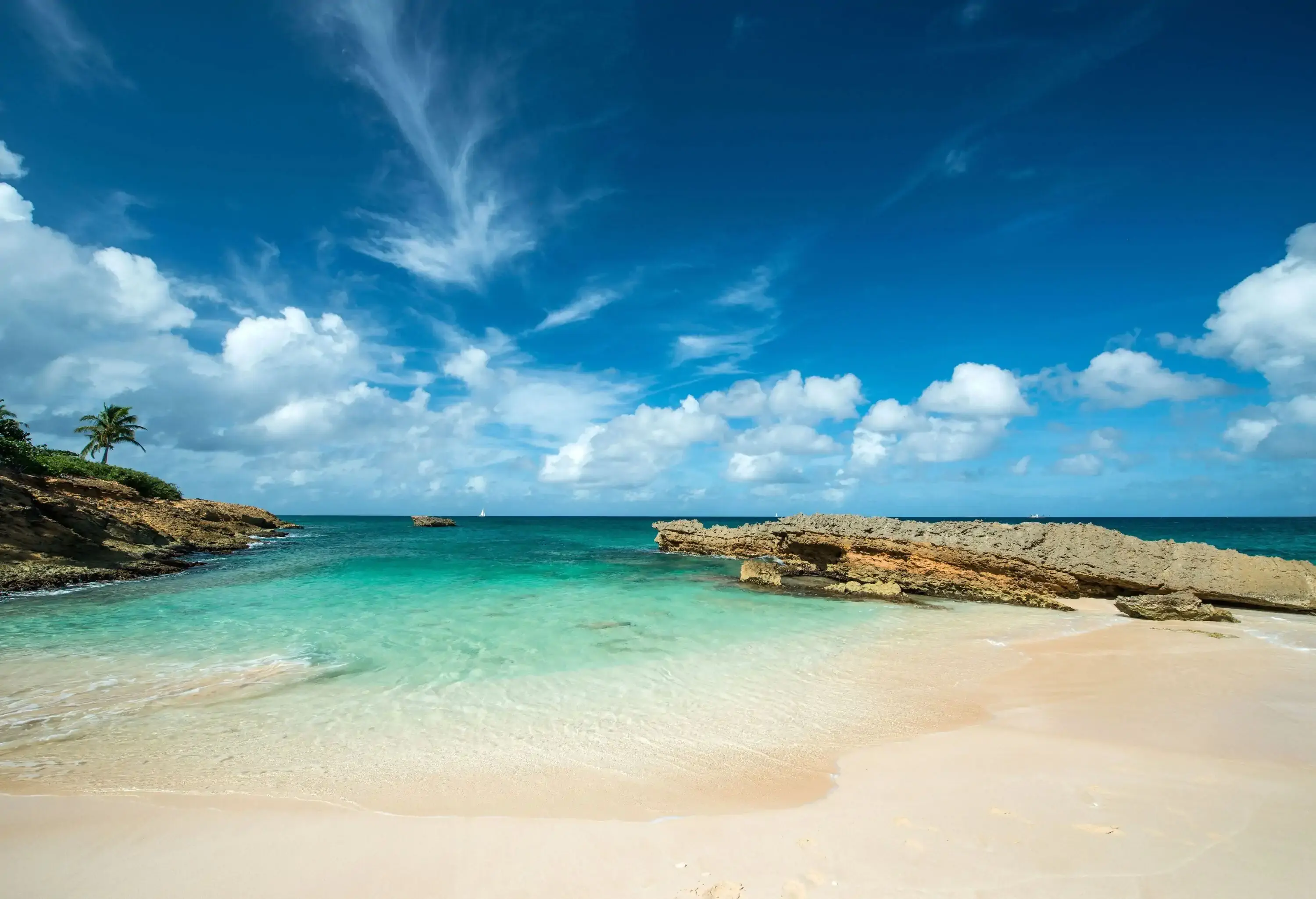 A scenic shallow beach with crystal clear water on fine white sand surrounded with rugged rocks.