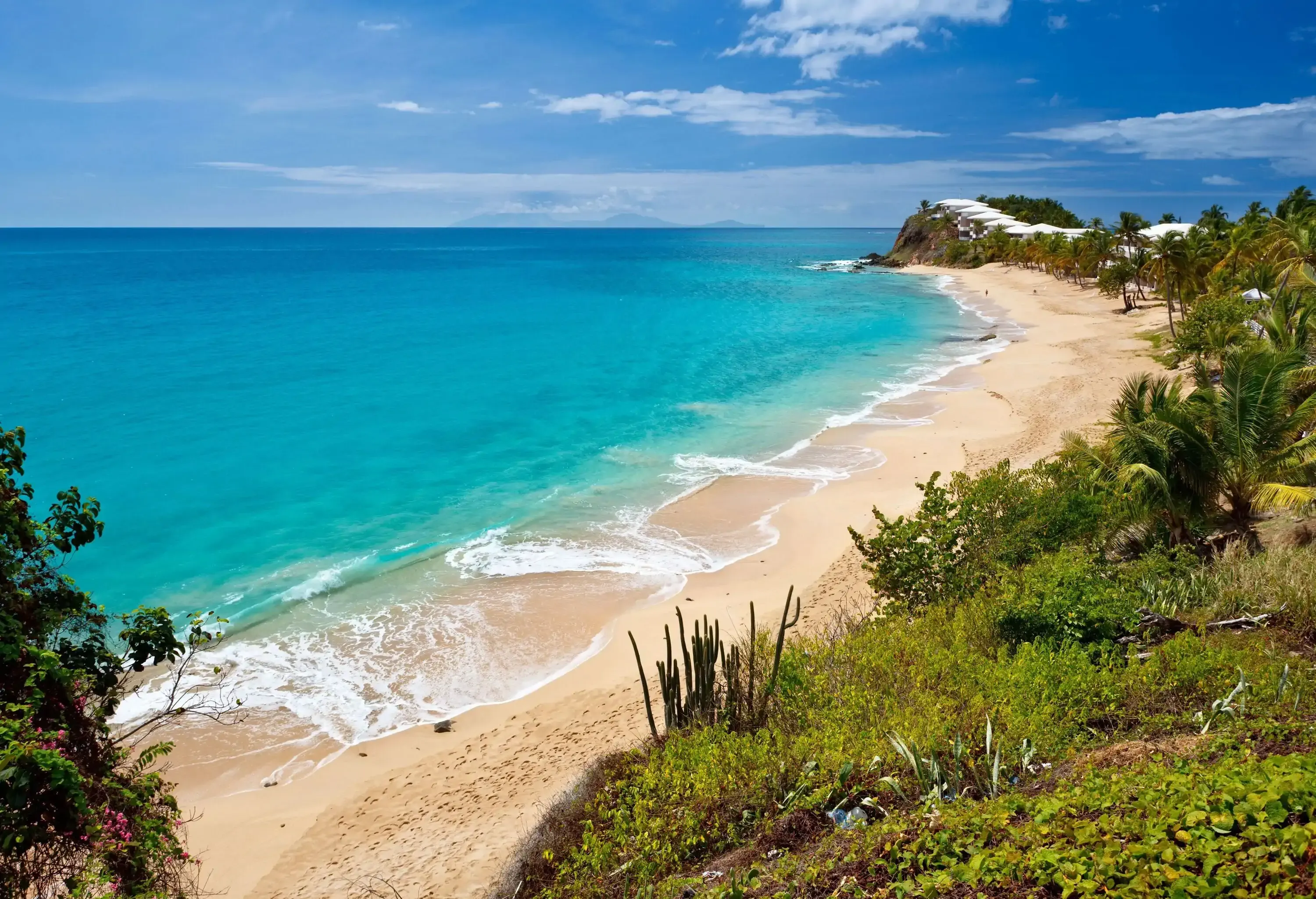 Aerial view of a lush island with a sandy shore surrounded by the blue sea against the cloudy blue sky.
