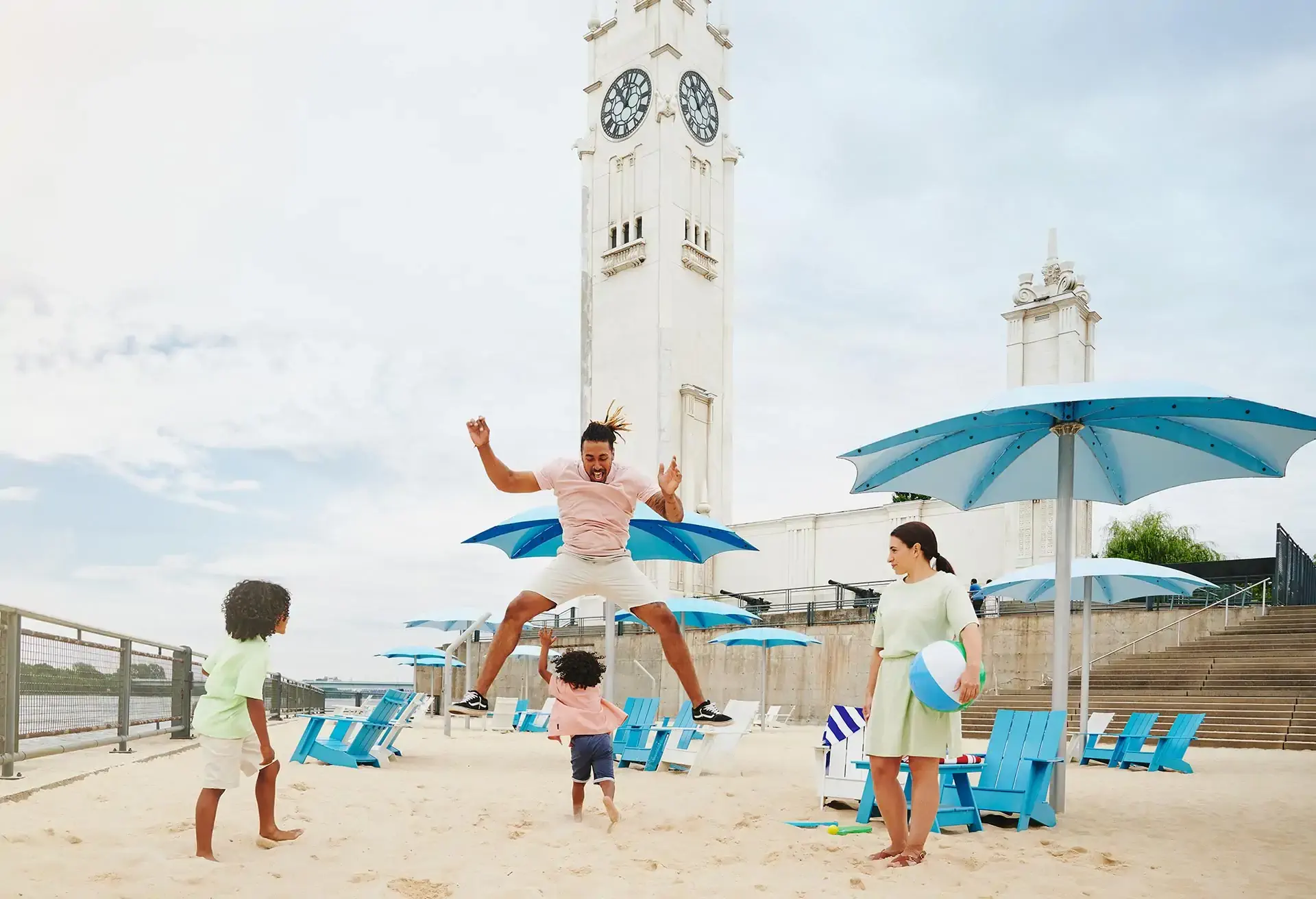 Family playing on a sandy beach with a clock tower and blue umbrellas