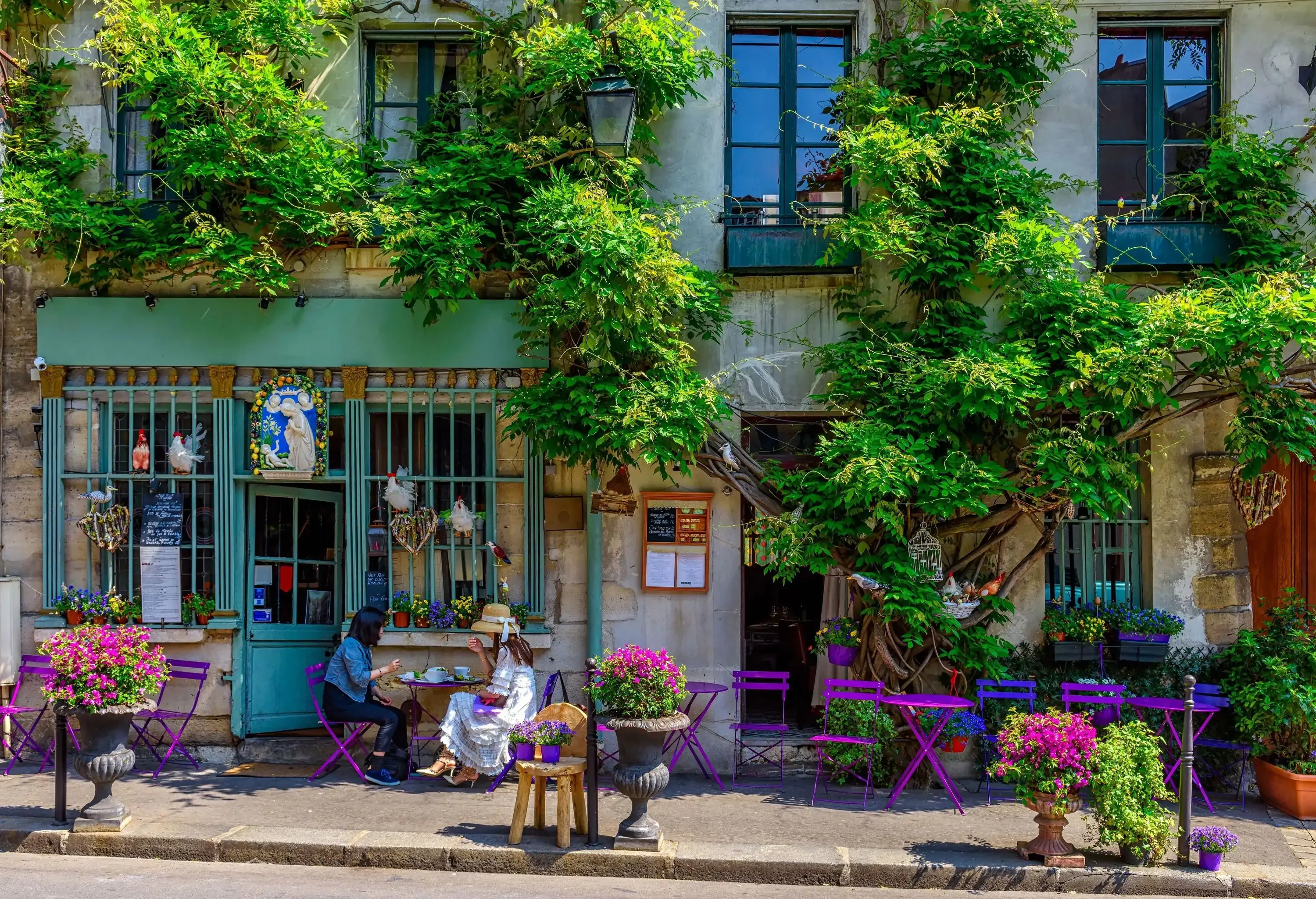 Outdoor dining on purple and blue painted tables and chairs along a pathway outside a local cafe.