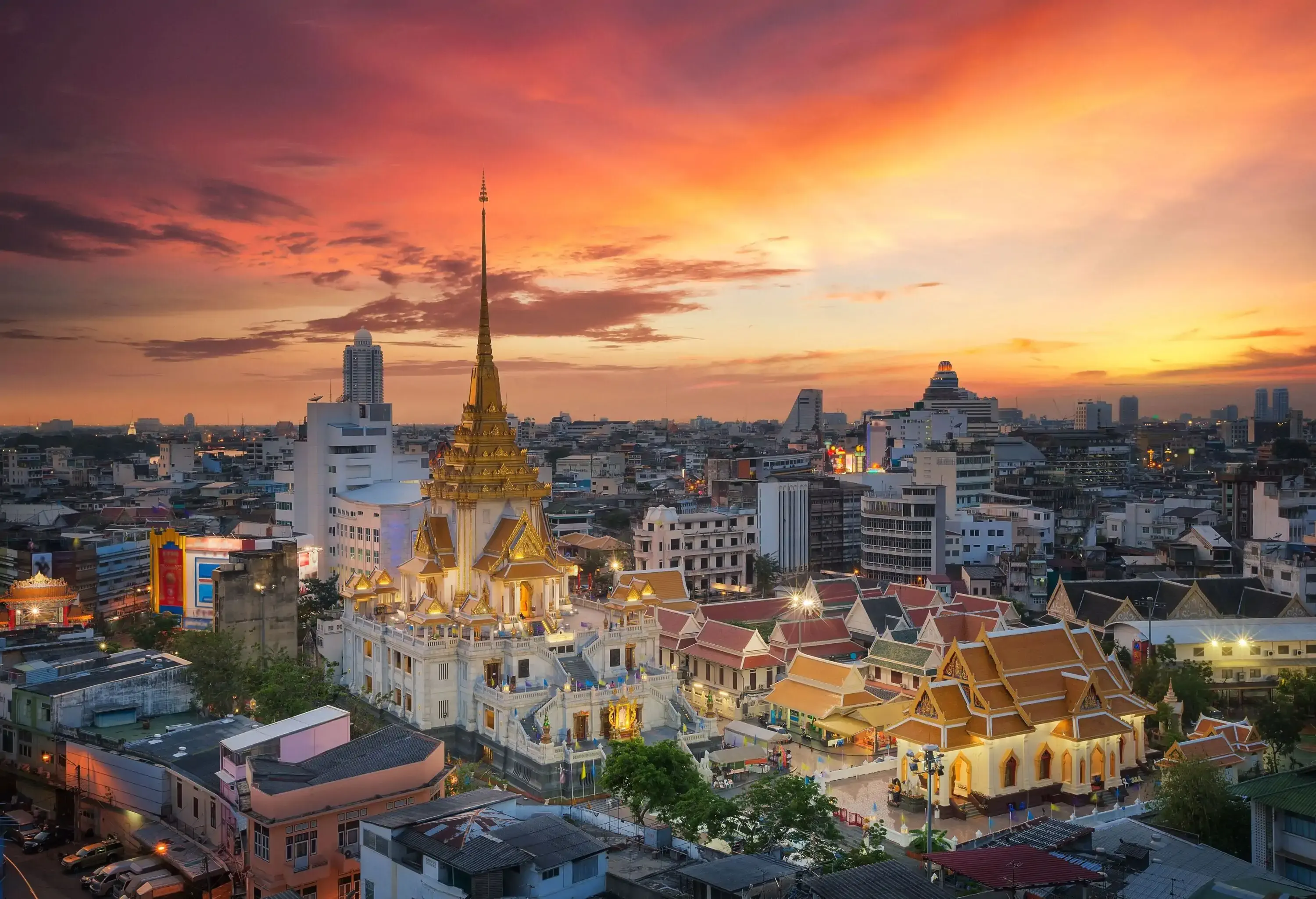Aerial view of a brightly lit Thai Buddhist temple in the centre of urban cityscape during dusk.