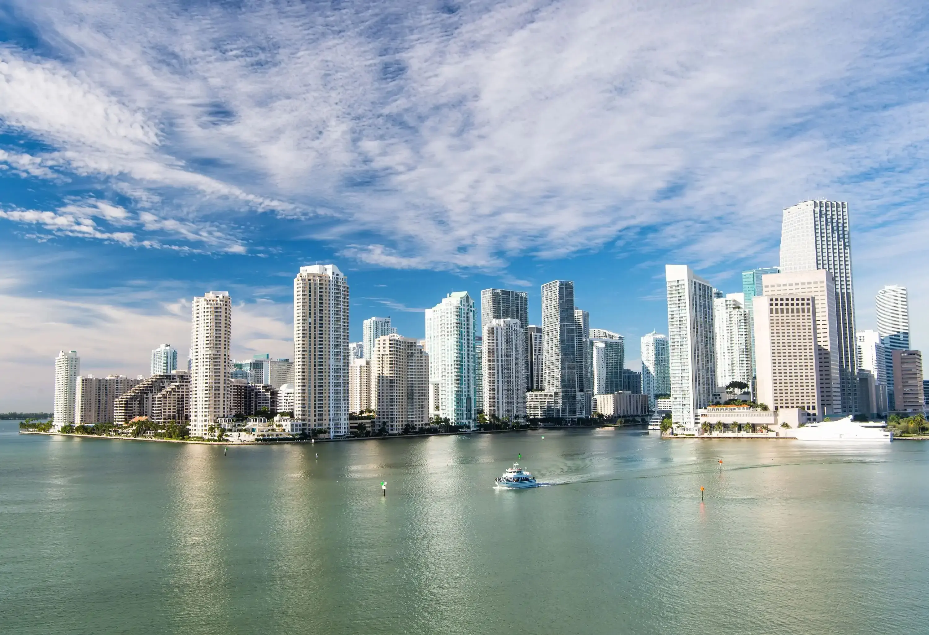 Miami's impressive skyscrapers reach for the sky against a backdrop of a blue, cloudy sky, while a white boat gracefully sails alongside the iconic downtown.