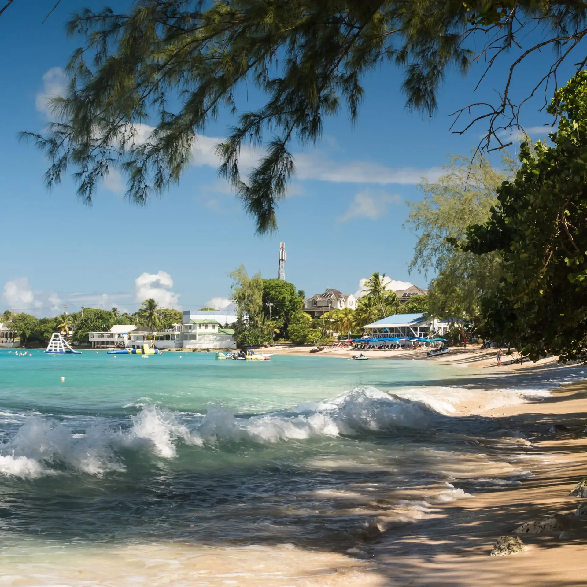 Beautiful tropical beach with turquoise water, white waves, and lush green trees.