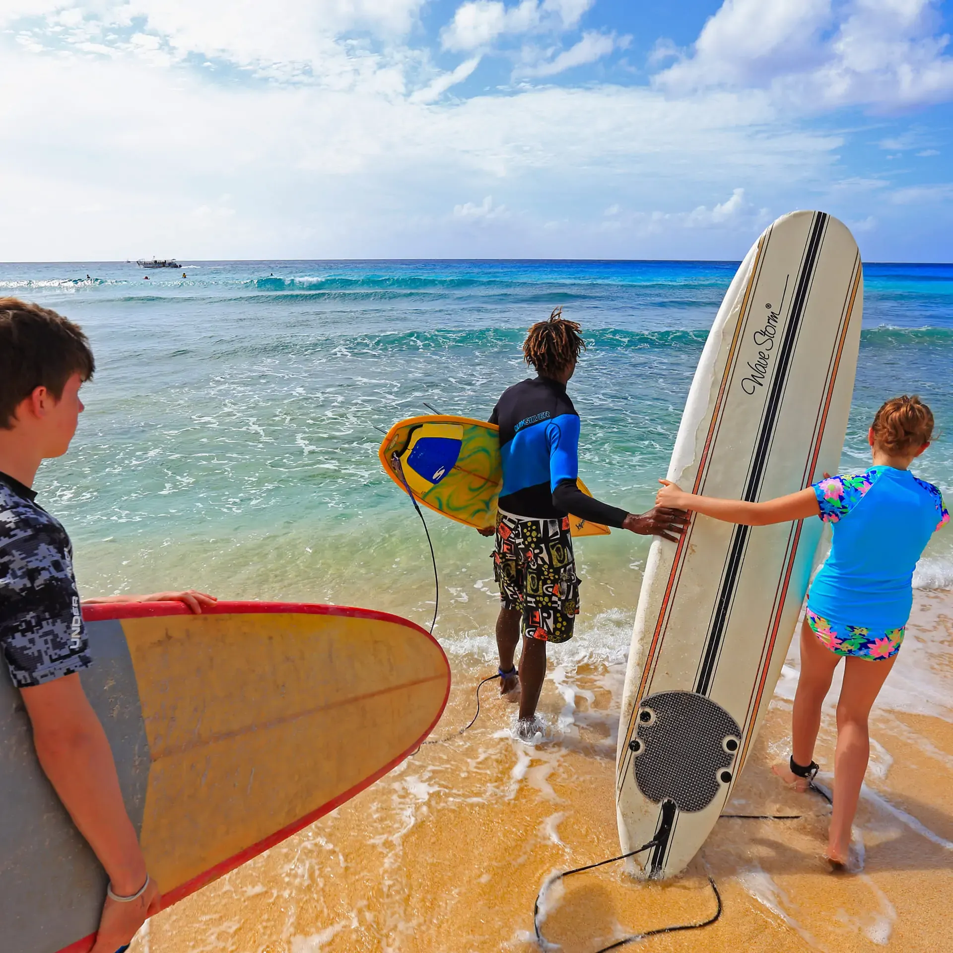 Three surfers holding their boards while heading into the ocean on a bright, sunny day.