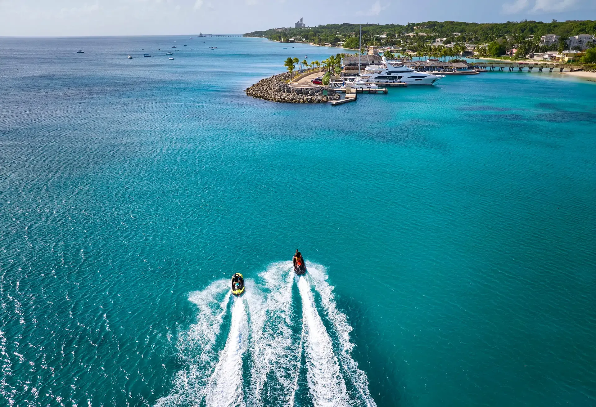 Two jet skis speeding across vibrant turquoise water toward a tropical coastline.