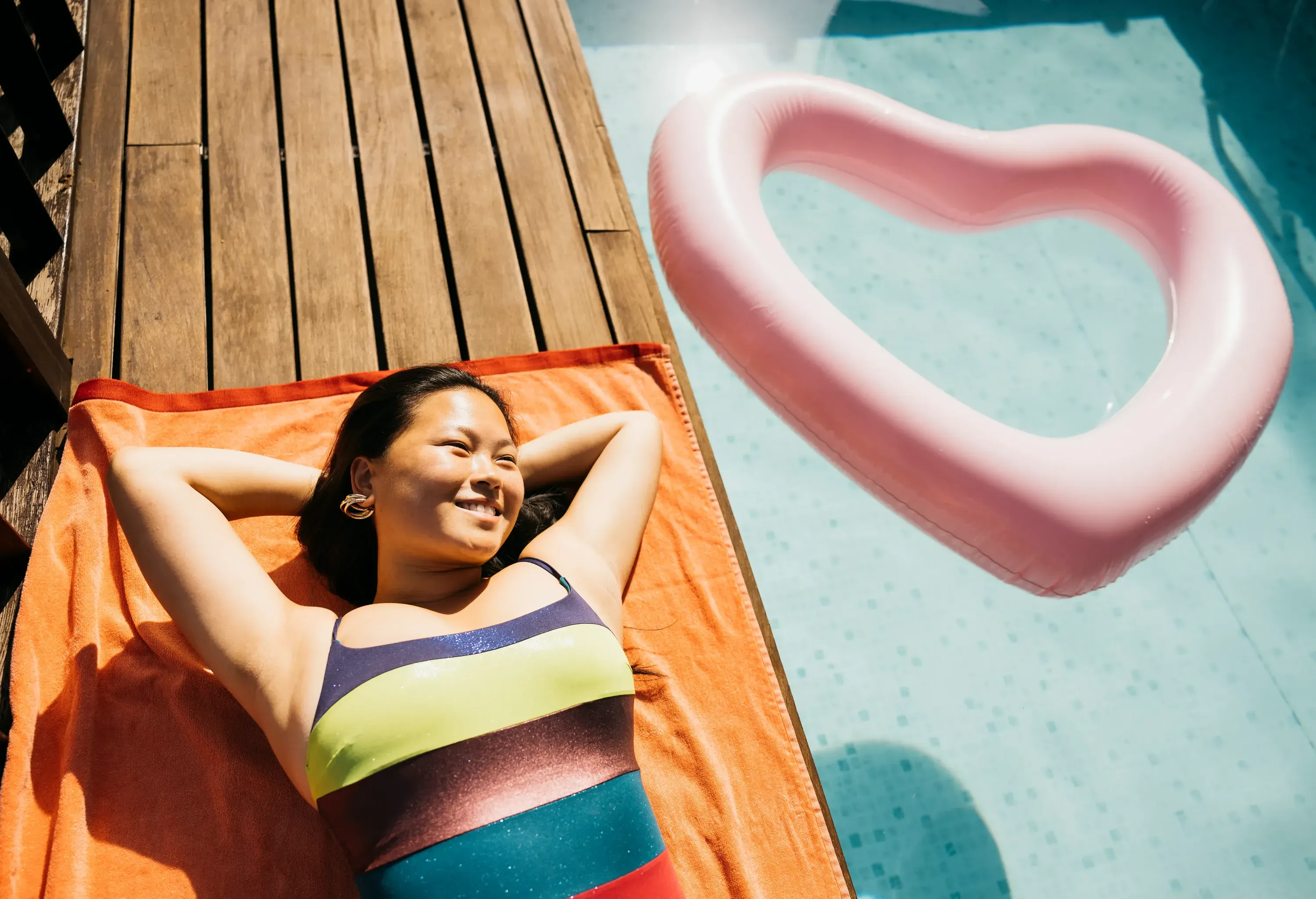 Portrait of young smiling woman wearing swimsuit, lying on a towel at poolside. Woman hanging out on a pool during summer vacations