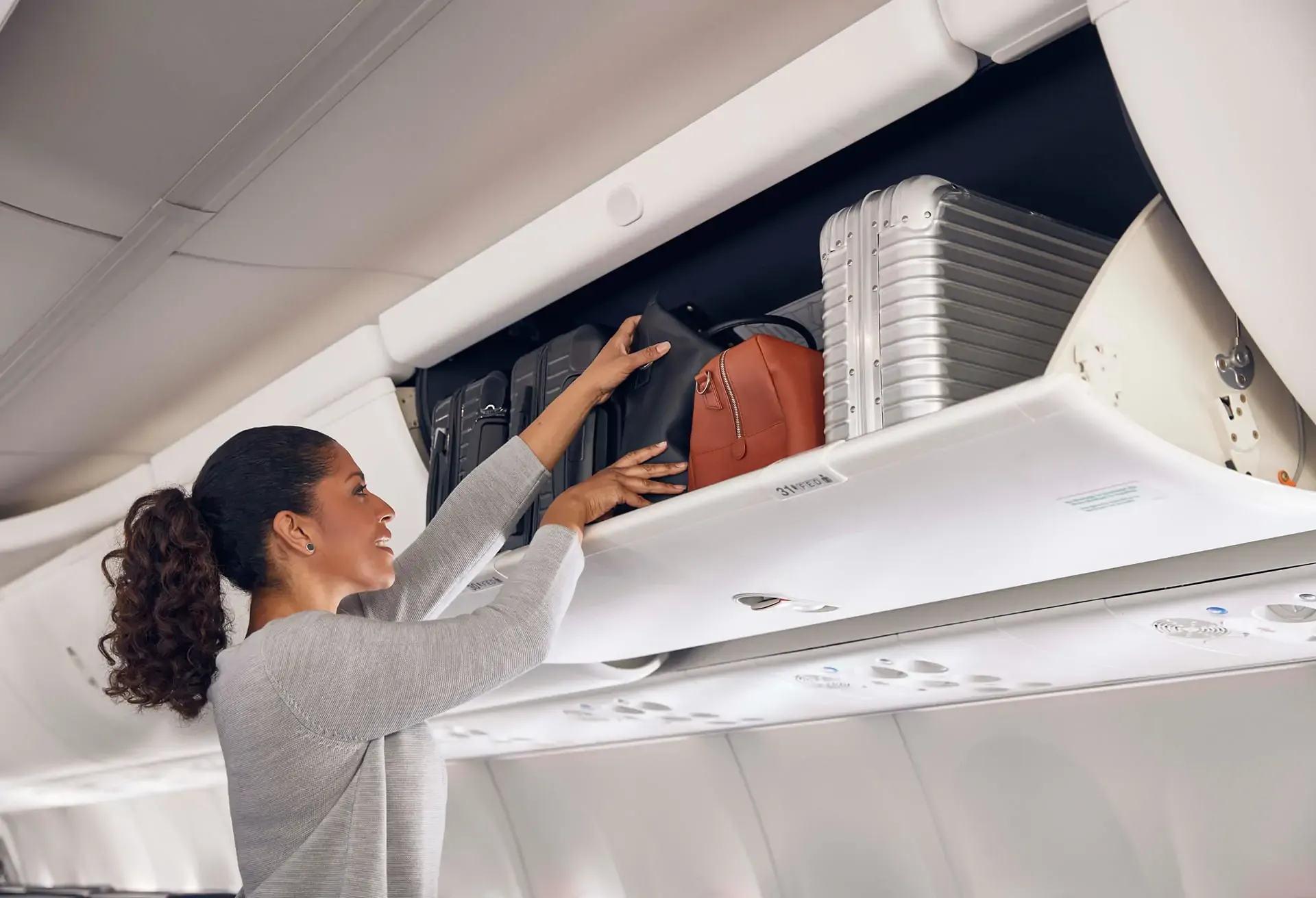 A woman placing her luggage into an overhead bin inside an airplane cabin.