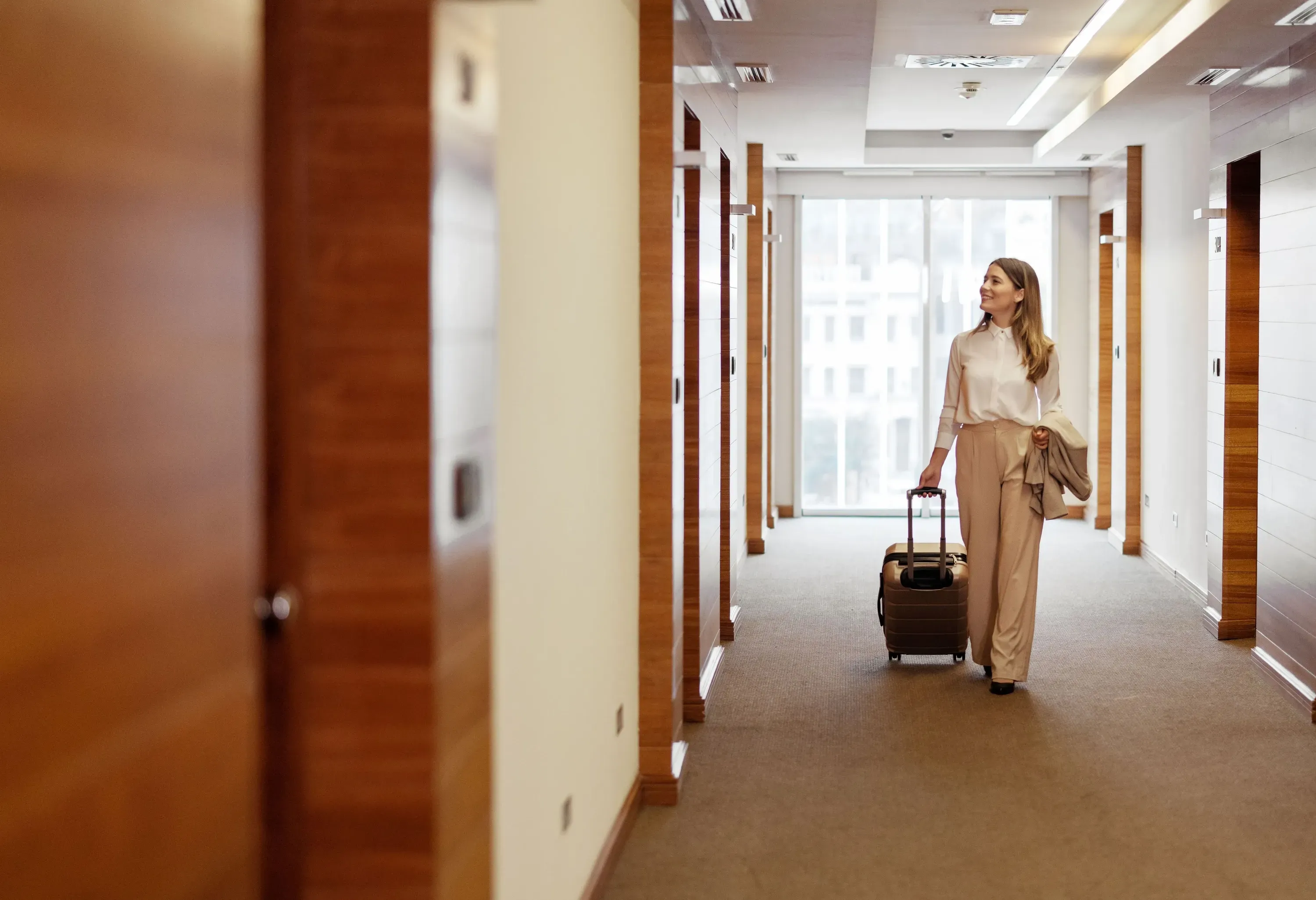 Elegant Business Lady in the Hallway of Hotel Room With Travel Trolley Luggage. Female Executive With Suitcase in Work Related Business Trip