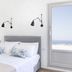 Aplai Dome in Oia bedroom with white bed and wall lamps, plus a door opening to sea views