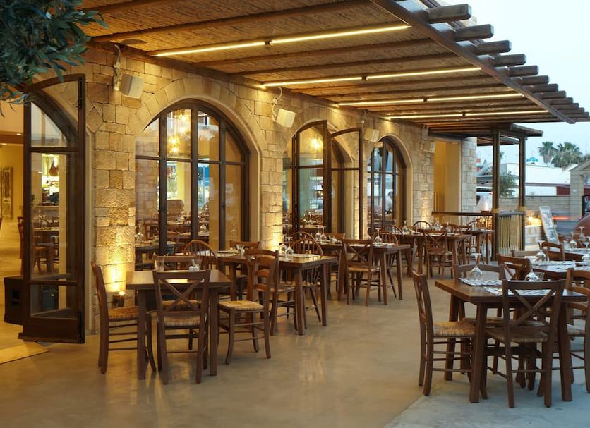 Outdoor terrace dining at Melpo Antia Hotel & Suites in Ayia Napa with wooden tables and arched windows