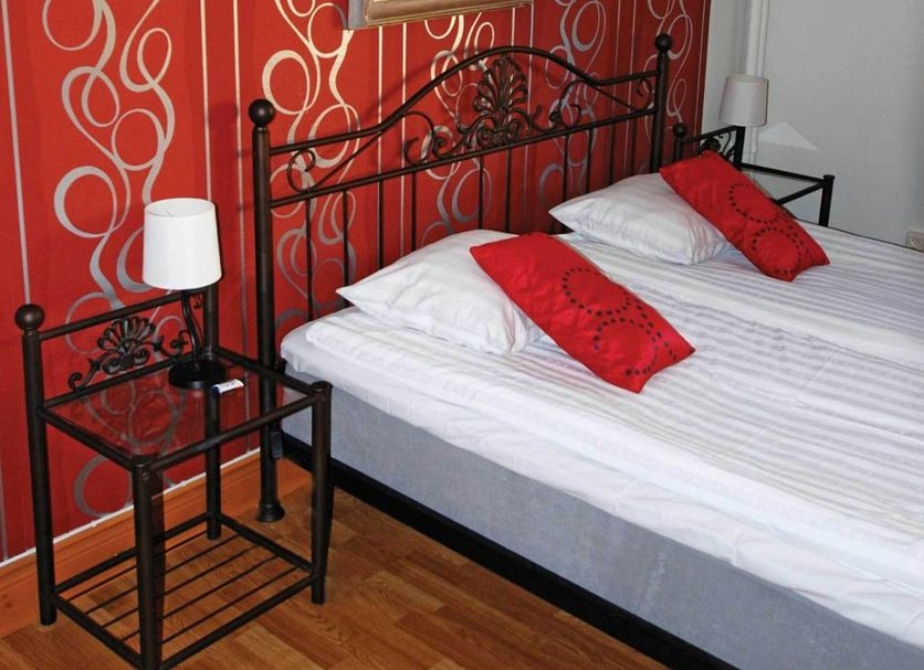 Avesta Stadshotell room with wrought iron bed, red patterned wall, and wood floor in Avesta