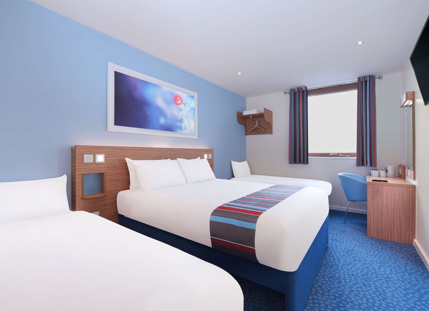 Travelodge Hull Central in Hull room with two beds, blue walls, window, desk, and wall-mounted TV