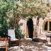 Refugio Del Pintor in Tilcara: shaded courtyard with tree, rustic stone wall, chairs and arched doorway
