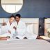 Hotel SLC in Murray: couple in robes sitting on a neatly made bed beside bedside lamps and a round mirror