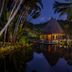 Anantara Maia Seychelles Villas in Anse Boileau, thatched overwater villa reflected in tropical lagoon at dusk
