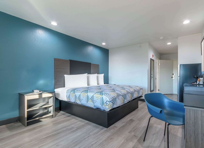 Studio 6 Suites Perris, CA guest room with king bed, desk, TV and blue accent wall
