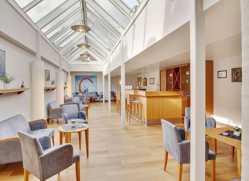 Hotel Pinenhus in Glyngøre: bright skylit lounge with gray armchairs, tables, and a wooden bar