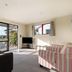 Kaikoura TOP 10 Holiday Park living area with sofa, TV, sliding door to outdoor deck and garden view