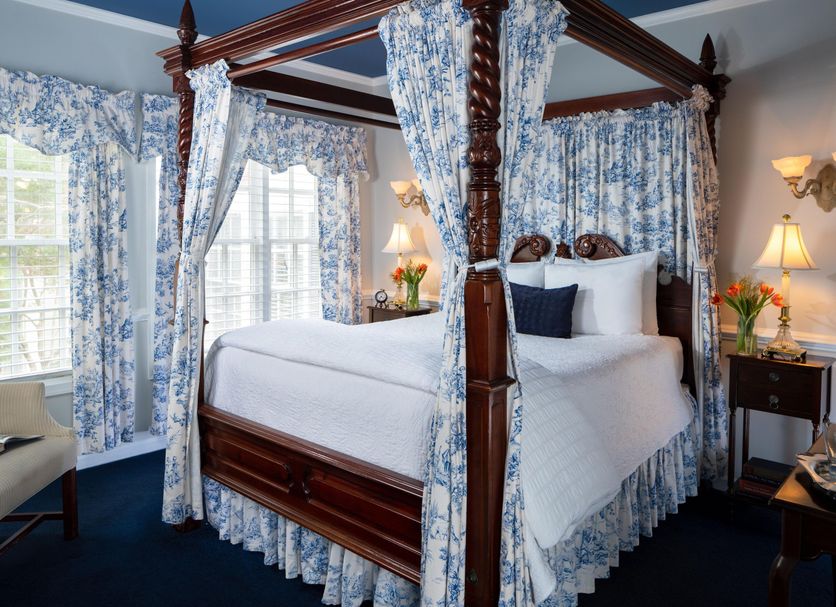 A Williamsburg White House Inn canopy bed with floral curtains and sitting area in Williamsburg