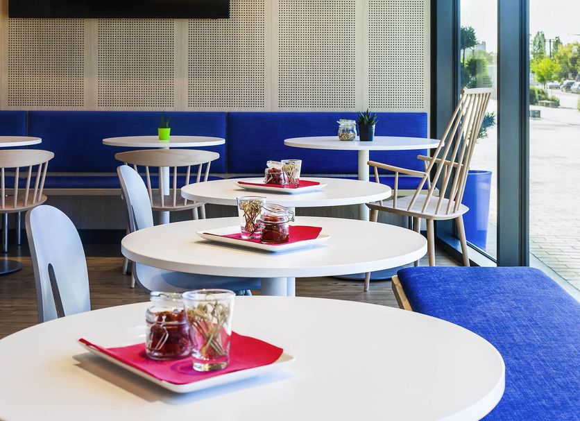ibis Styles Mulhouse Centre Gare lounge with white tables, blue benches and large window view