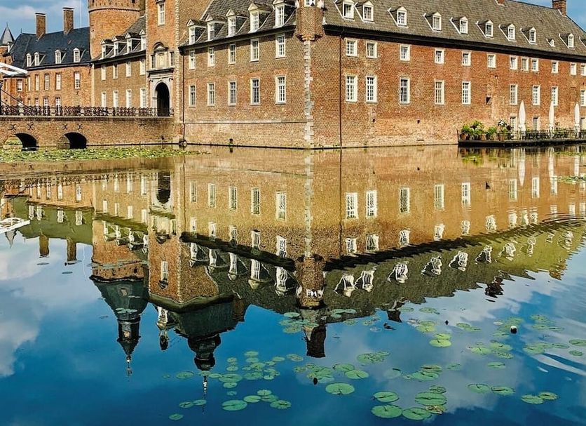 Romantik Parkhotel Wasserburg Anholt in Isselburg reflected in a calm moat beside a historic brick castle