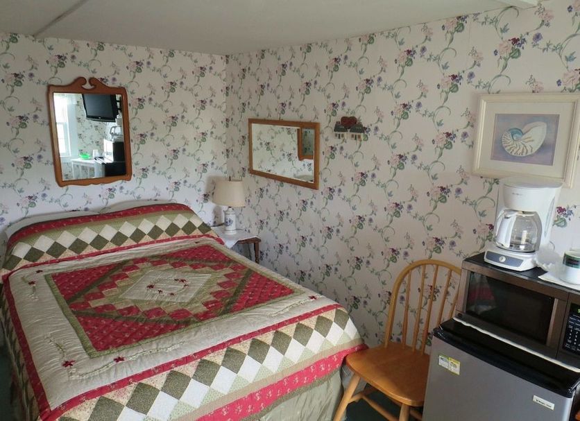 Windjammer BY The Sea room with floral wallpaper, quilted bed, chair, and mini fridge in Hampton