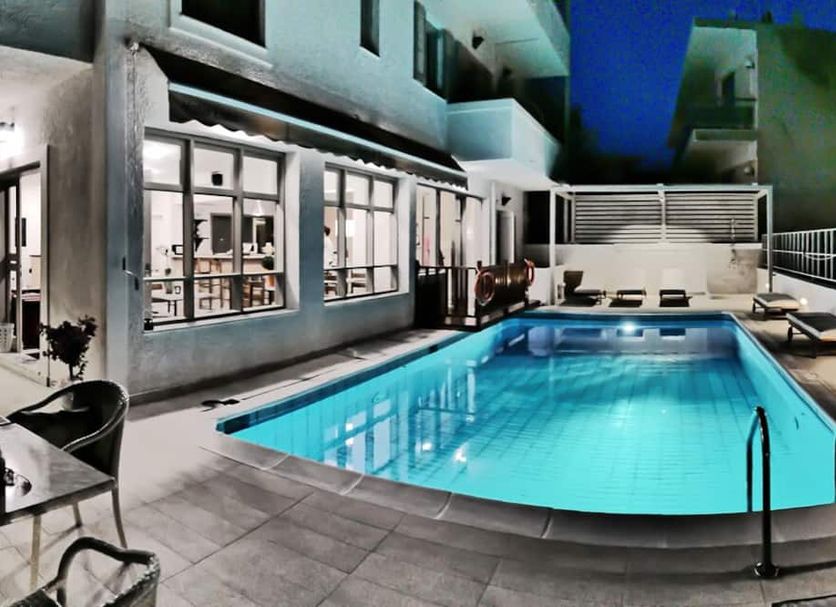 Erato Hotel in Agia Marina with a lit outdoor pool beside a modern building and lounge chairs
