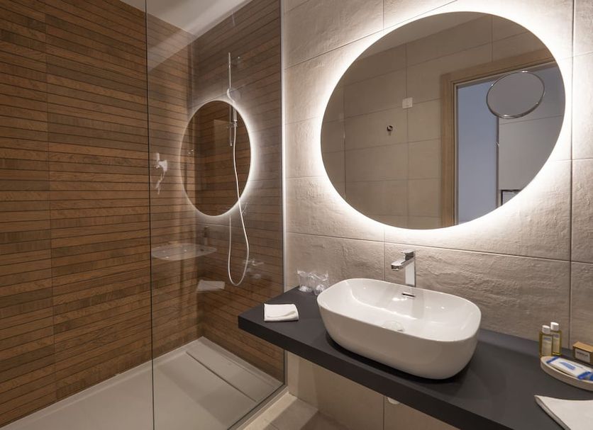 Hotel Montenegro bathroom in Budva with vessel sink, round backlit mirror and wood shower wall