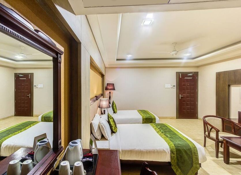 Treebo Shivani, Indore: bright hotel room with two beds, mirror, chairs, and a bedside lamp
