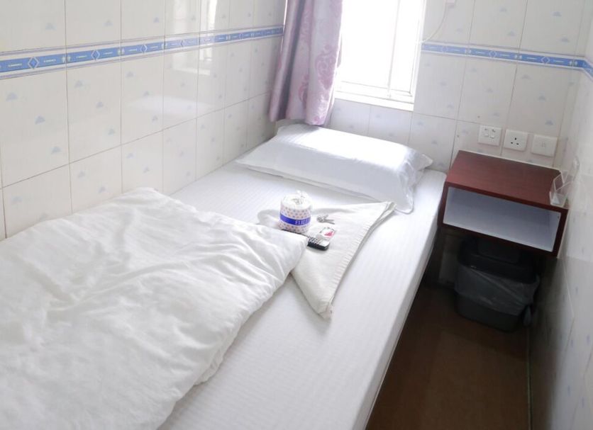 Garden Guest House in Hong Kong features a compact single bed beside a small bedside table and window.