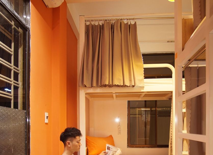 Guest reading in a rocking chair at City Hostel Da Nang, with a bunk bed and warm orange walls