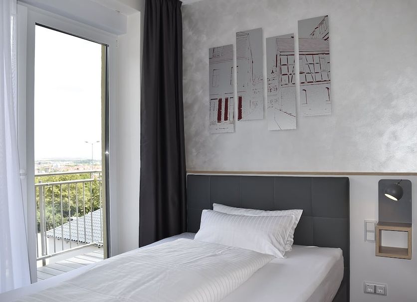 Hotel am Waldkasino in Erfurt: bright guest room with bed, wall art, and balcony door to city view