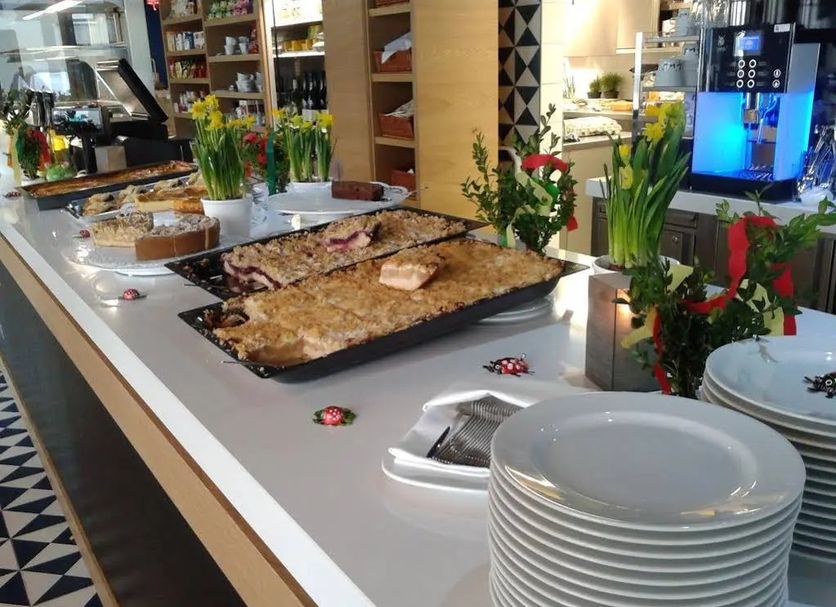 Claudius Hotel Bochum buffet counter with trays of food, stacked plates, and floral decor