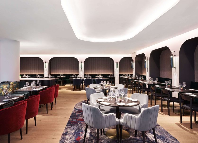 Hyatt Regency London Stratford dining room with round tables, red chairs and arched window seating