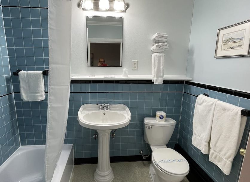 Bucksport Inn bathroom with blue tile walls, pedestal sink, tub-shower, and white towels in Bucksport