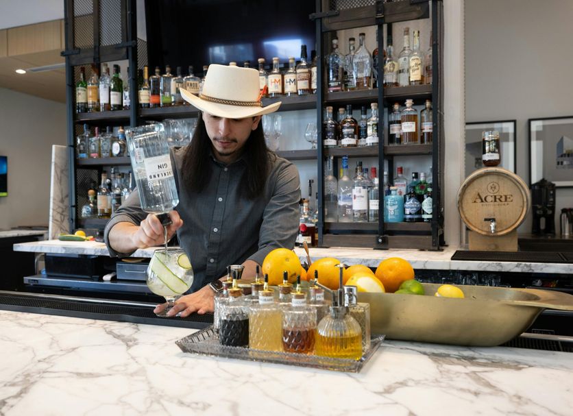 AC Hotel Fort Worth Downtown bartender preparing a cocktail at a marble bar with citrus and bottles